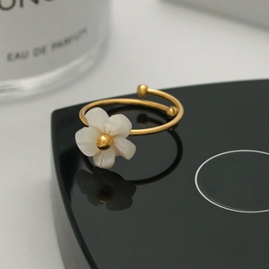 Detail of a floral gold ring with white shell petals on a reflective black display stand
