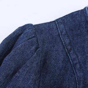 Details eines blauen Jeanskleides mit Schulternähten und Falten an den Manschetten