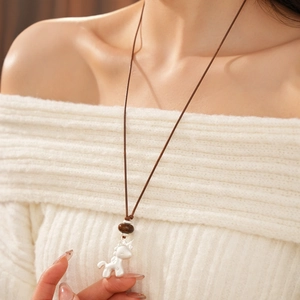 Détail d'un pendentif licorne mat sur cordon en cuir marron porté avec un pull blanc