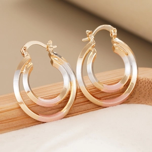 Close-up of tricolor double hoop earrings with gold, silver and pink finish on bamboo