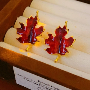 Detailed macro of vintage red maple leaf earrings with gold trim in a classic jewelry box
