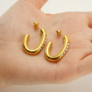 Close-up of gold U-shaped earrings with inlaid pearls held in a person's palm