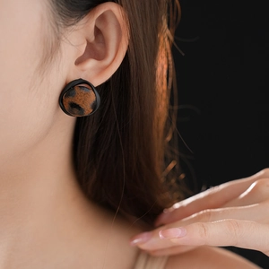 Détail de boucles d'oreilles léopard avec bordure noire portées sur le lobe