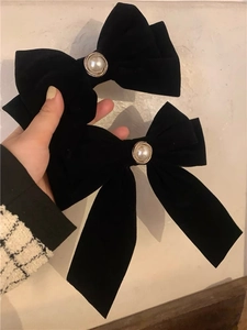 Detail view of black velvet bow hair clips with pearls and long flowing ribbons