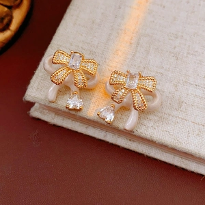 Detailed view of silver needle bow earrings with zircon stones on a woven texture