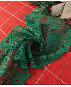Detail of green lace Christmas table runner with intricate floral patterns on plaid background