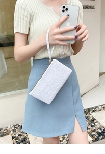 Detailed macro of white crocodile-embossed leather clutch with gold zipper and wrist strap
