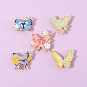Five butterfly enamel pins with floral patterns and gold metal edges on purple background