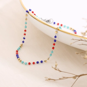 Macro shot of colorful cylindrical beads on a slim silver chain draped over a white bowl