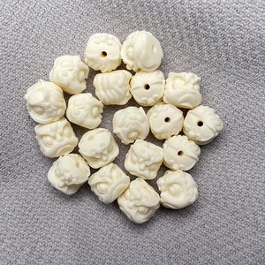 Carved ivory nut lion head beads for jewelry making displayed on a grey fabric