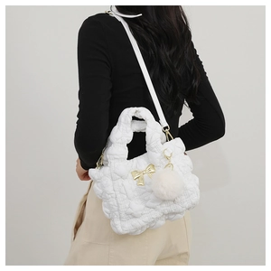 Detail of white quilted nylon bag with golden bow ornament and fluffy pompom charm