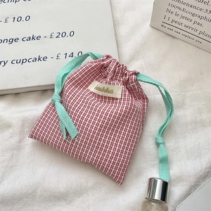 Detail of red gingham cotton drawstring pouch with green ropes and logo patch