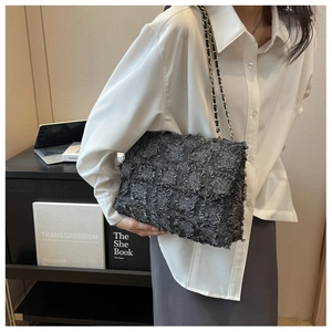 Detail of dark grey tweed crossbody bag featuring a golden chain strap and woven texture
