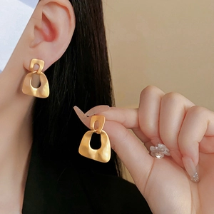 Close-up of golden geometric earrings with a matte brushed texture on earlobe