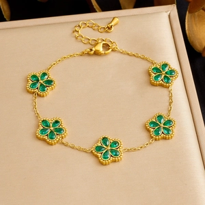 Dettaglio di un bracciale dorato con ciondoli a fiore in zircone verde su velluto champagne