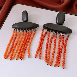 Detail of ethnic style wooden earrings with vibrant orange beaded tassels and silver needles