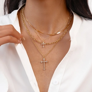 Close-up of layered gold cross necklaces with sparkling crystals on a white shirt