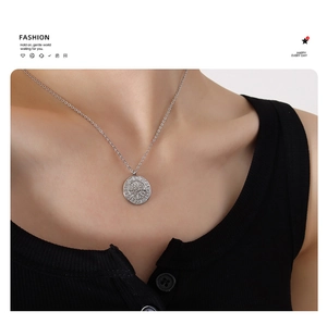 Detailed view of silver zodiac medallion necklace worn on a ribbed knit top