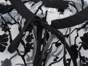 Detail of sheer mesh fabric with black flocked floral pattern and neck tie lace-up