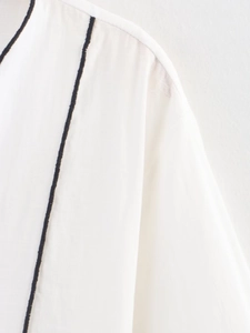Details der weißen Stoffstruktur mit eleganter schwarzer Kontrastpaspel an der Schulter