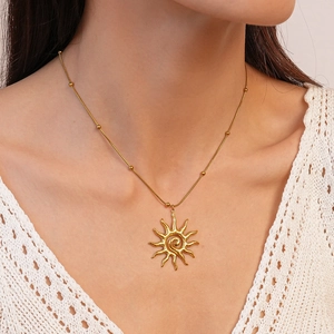 Close-up of golden sun swirl pendant necklace with small beads on a snake chain