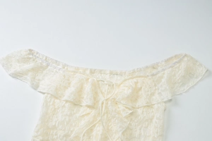Close-up of white lace off-shoulder top with floral patterns and drawstring tie detail