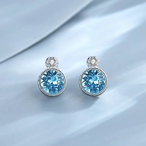 Elegant round blue gemstone stud earrings with silver metal on wavy blue fabric