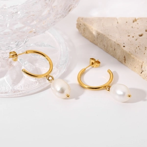 Detailed close-up of gold hoop earrings with white teardrop pearl pendants on white stone
