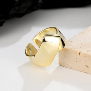Detailed close-up of wide gold geometric folding open ring resting on a light stone