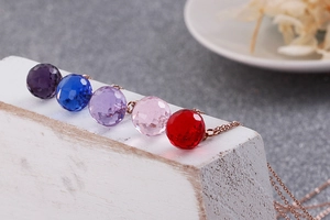 Detailed macro view of faceted crystal sphere pendants in five vibrant colors on rose gold chains
