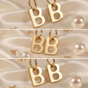 Elegant gold letter B drop earrings with high polish finish on satin background