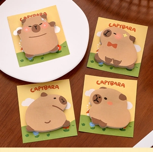 Close-up of four cute Capybara shaped sticky notes on a warm wooden desk background