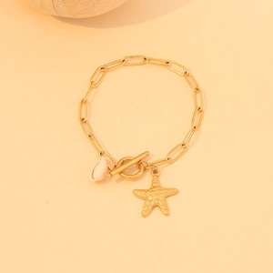 Close-up of golden starfish necklace with white shell bead on a warm beige surface