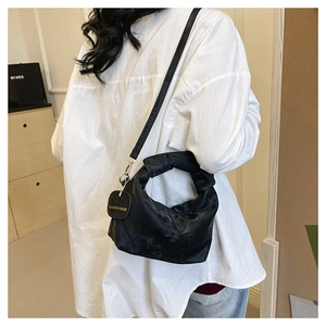 Detail of black crossbody bag with a unique knotted handle and branded round tag