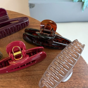 Grandi mollettoni per capelli in resina bordeaux e ambra su tavolo in legno scuro