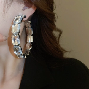 Close-up of oversized silver hoop earrings with square-cut crystal stones on a model