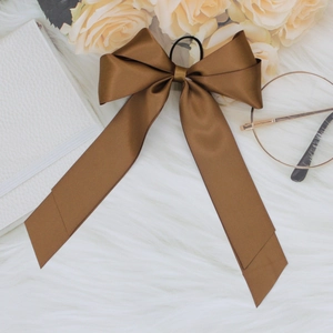 Detail of elegant coffee brown satin bow hair clip with long ribbons on plush background