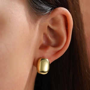 Close-up of minimalist gold-plated oval stud earrings worn on a model's ear