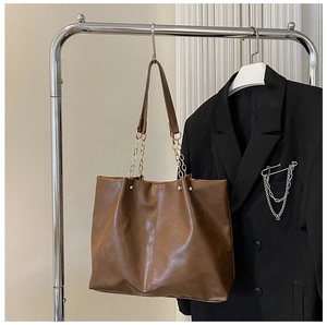 Détail d'un sac cabas en cuir marron avec bandoulière chaîne dorée sur support en métal