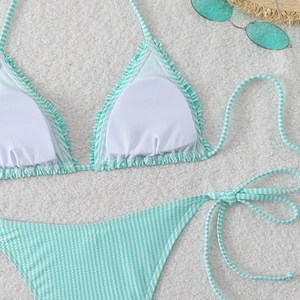 Flat lay of a mint green striped bikini set with ruffled edges on a soft white plush background