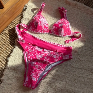 Dettaglio bikini a vita alta rosa con motivi floreali bianchi e bordi smerlati eleganti