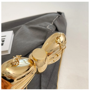 Detail of a shiny gold bow-shaped metal evening bag with a delicate chain strap