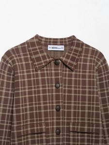 Detailaufnahme der braun karierten Strickjacke mit eckigem Ausschnitt und Knöpfen