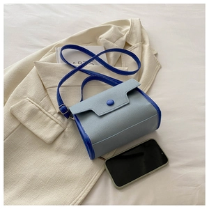 Top view of blue textured leather handbag on a beige blazer with shoulder strap detail