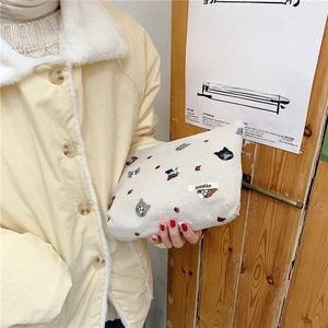 Detail view of cream canvas makeup bag featuring cat embroidery and side brand label