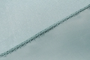 Detailed close-up of light blue satin fabric texture with precise diagonal stitching seam