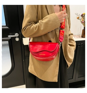 Detail of red PU leather saddle bag featuring a wide patterned strap and gold lettering