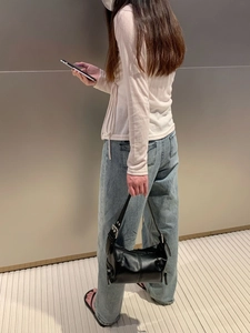 Model holding a black leather underarm bag with silver hardware and zipper detail