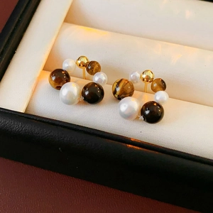 Detail of round pearl and tiger eye stone stud earrings in a luxury jewelry box