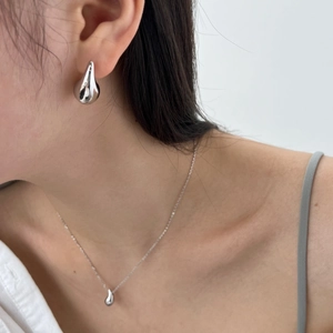 Close-up of minimalist silver water drop earring and matching pendant necklace on model